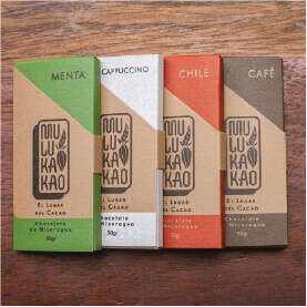 Four chocolate bars in paper packaging are artfully arranged on a wooden surface, embodying the essence of artisan cacao and coffee. The packages, labeled Menta, Cappuccino, Chile, and Café, shimmer in distinct hues of green, white, red, and brown respectively.