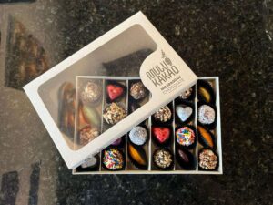 A box of assorted handmade chocolates from local favorite Odullu Kakao—a chocolate shop known for heart-shaped treats—sits on a dark granite countertop, perfect to pair with your favorite local coffee or enjoy at your go-to Hattiesburg cafe.